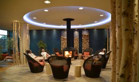 Drei Gäste sitzen um den Kamin im oberen Ruheraum des Saunagartens