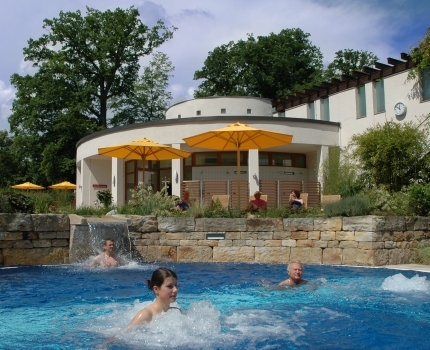 Drei Gäste befinden sich Saunapool, drei Gäste entspannen auf Liegestühlen im Saunagarten