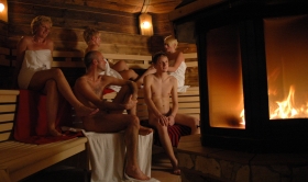 Fünf Gäste sitzen um den Kaminofen in der Saunakabine - Erdsauna im Saunagarten