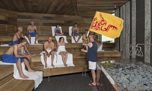 Acht Gäste sitzen in der Saunakbine, während ein Mitarbeiter mit der Aufgussfahne arbeitet - Birkensauna